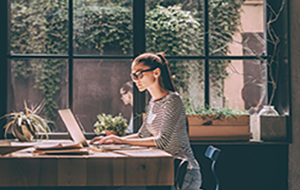  Young woman sits at desk in front of window working on laptop