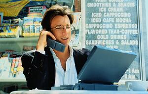 Man sits in café working on laptop and speaking on cell phone. The devices date the scene to the late 1990s